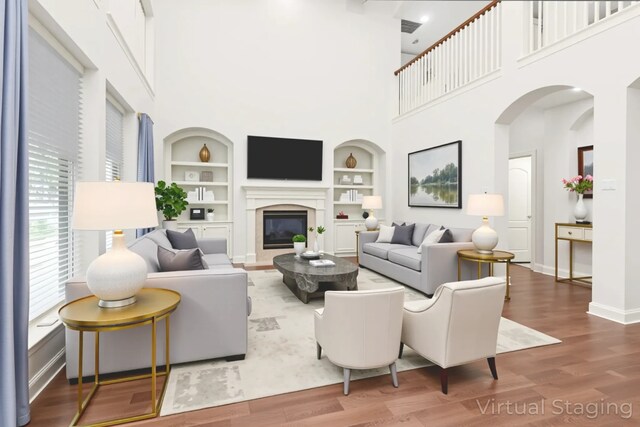 14015 Halprin Creek Dr, Cypress, TX 77429 - living room featuring built in features, wood finished floors, a glass covered fireplace, a towering ceiling, and arched walkways