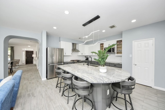7619 Park Sage Ln, Cypress, TX 77433 - kitchen with appliances with stainless steel finishes, wall chimney exhaust hood, arched walkways, a breakfast bar area, and light wood-type flooring