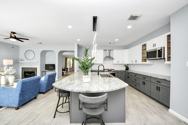 7619 Park Sage Ln, Cypress, TX 77433 - kitchen featuring stainless steel microwave, gray cabinets, wall chimney exhaust hood, a breakfast bar area, and tasteful backsplash