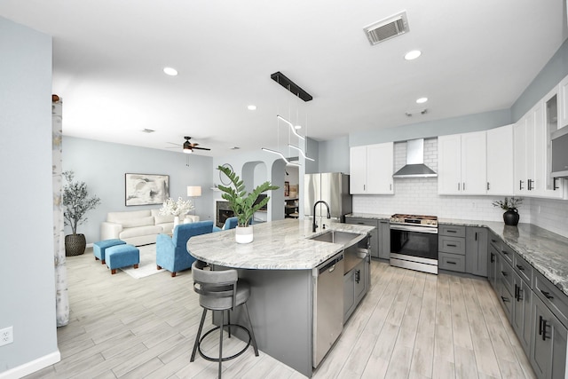 7619 Park Sage Ln, Cypress, TX 77433 - kitchen with appliances with stainless steel finishes, wall chimney exhaust hood, gray cabinets, ceiling fan, and a kitchen breakfast bar