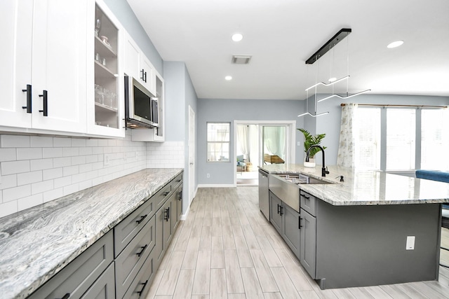 7619 Park Sage Ln, Cypress, TX 77433 - kitchen with stainless steel appliances, gray cabinets, decorative backsplash, light stone countertops, and glass insert cabinets