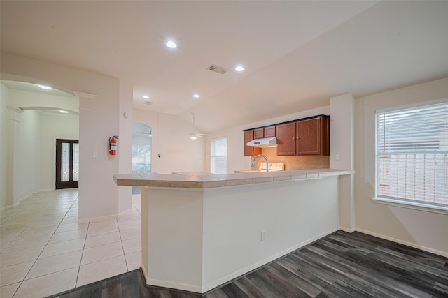 5515 Brookhollow Pines Ct, Houston, TX 77084 - kitchen with tile counters, a peninsula, arched walkways, a ceiling fan, and light wood-type flooring