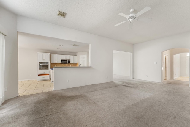 5723 Painted Trail Dr, Houston, TX 77084 - unfurnished living room featuring arched walkways, light colored carpet, a textured ceiling, a ceiling fan, and light tile patterned floors