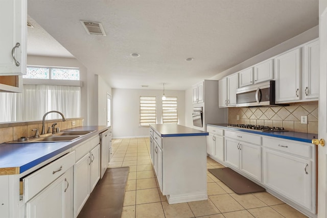 5723 Painted Trail Dr, Houston, TX 77084 - kitchen with stainless steel appliances, a kitchen island, backsplash, white cabinetry, and light tile patterned floors