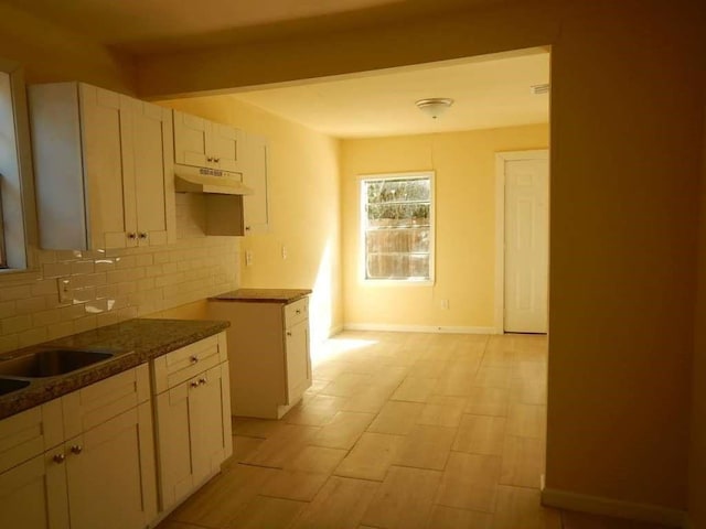 7121 Conley St, Houston, TX 77021 - kitchen with under cabinet range hood, decorative backsplash, dark countertops, and white cabinetry