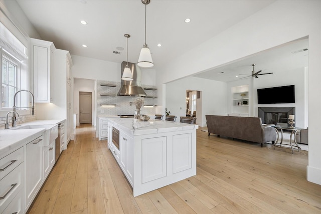 6626 Westchester Ave, West University Place, TX 77005 - kitchen featuring wall chimney exhaust hood, stainless steel microwave, ceiling fan, white cabinets, and tasteful backsplash