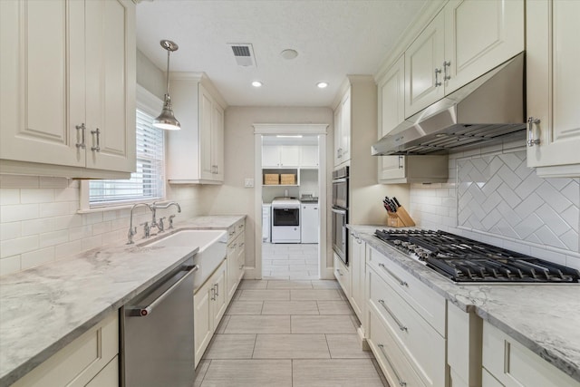 2603 Haverhill Dr, Houston, TX 77008 - kitchen featuring stainless steel appliances, under cabinet range hood, washer and clothes dryer, hanging light fixtures, and decorative backsplash