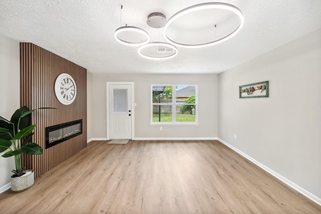 11114 Daybreak Ln, Cypress, TX 77429 - unfurnished living room featuring wood finished floors, a glass covered fireplace, and a textured ceiling