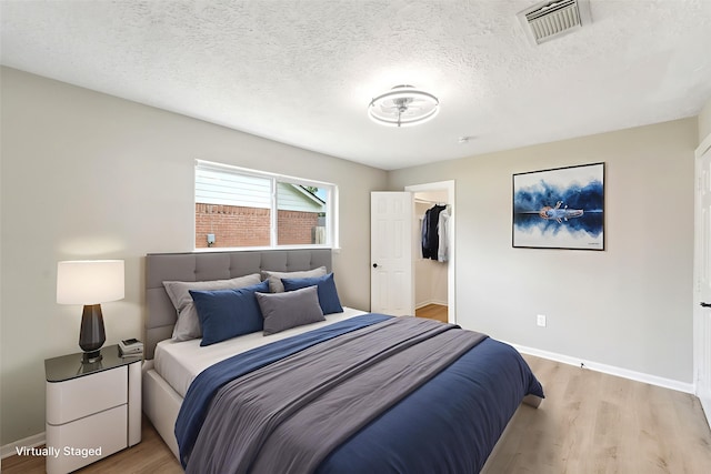 11114 Daybreak Ln, Cypress, TX 77429 - bedroom with light wood finished floors, a walk in closet, and a textured ceiling
