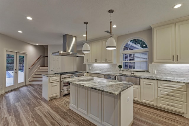 62 N Turtle Rock Ct, The Woodlands, TX 77381 - kitchen featuring wall chimney exhaust hood, appliances with stainless steel finishes, a center island, light wood finished floors, and backsplash