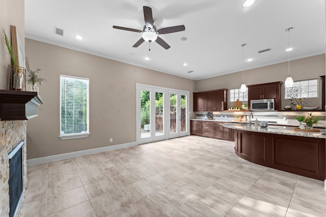 127 Benjis Pl, The Woodlands, TX 77380 - kitchen featuring stainless steel microwave, a ceiling fan, crown molding, a fireplace, and light stone counters