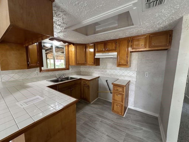6523 Hanley Ln, Houston, TX 77016 - kitchen with tile counters, under cabinet range hood, brown cabinetry, tasteful backsplash, and a textured ceiling
