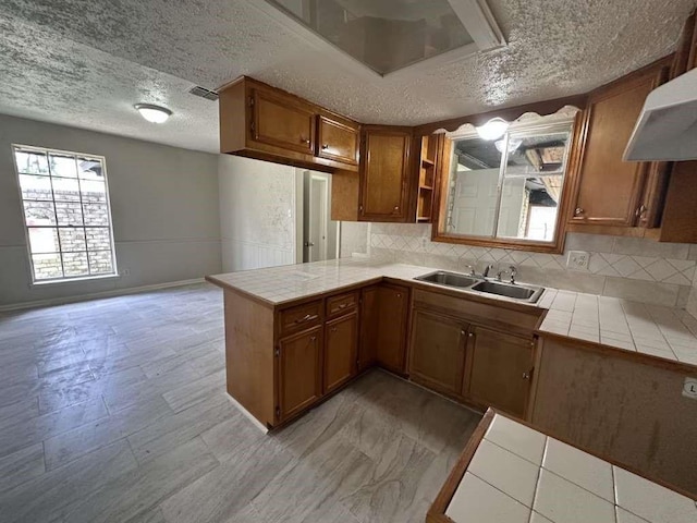 6523 Hanley Ln, Houston, TX 77016 - kitchen featuring tile counters, brown cabinets, a textured ceiling, decorative backsplash, and range hood