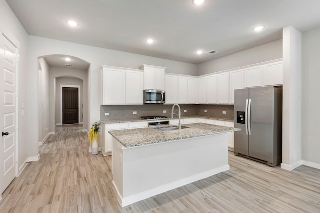 10005 Red Beadtree Pl, Conroe, TX 77385 - kitchen featuring stainless steel appliances, light wood-style floors, arched walkways, white cabinetry, and backsplash