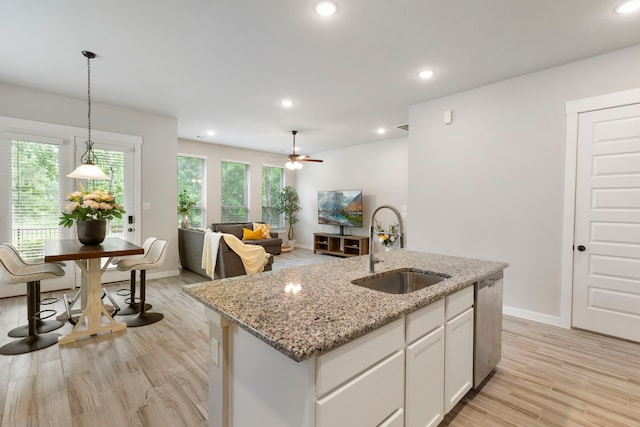 10005 Red Beadtree Pl, Conroe, TX 77385 - kitchen featuring a kitchen island with sink, light wood finished floors, white cabinets, pendant lighting, and light stone countertops
