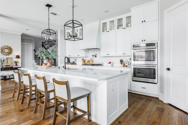 3239 Caney Dr, Katy, TX 77493 - kitchen featuring stainless steel double oven, custom range hood, glass insert cabinets, light countertops, and dark wood-style flooring