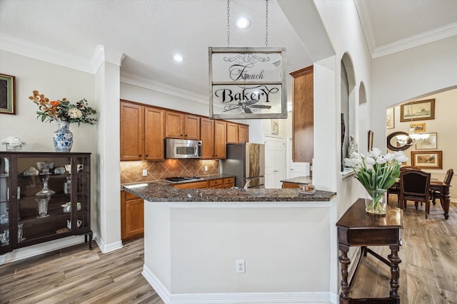 1607 N Primavera Dr, Pearland, TX 77581 - kitchen with appliances with stainless steel finishes, brown cabinets, arched walkways, light wood-style floors, and backsplash