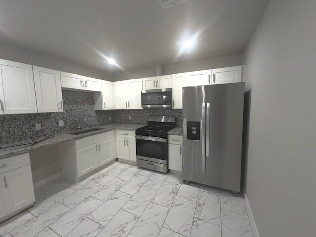 9013 Lugary Dr, Houston, TX 77074 - kitchen featuring stainless steel appliances, decorative backsplash, white cabinetry, and light marble finish flooring