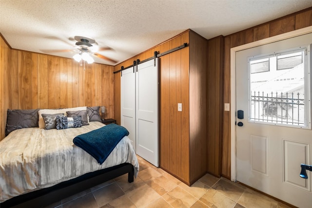 374 W Lake Shore Dr, Livingston, TX 77351 - bedroom with a barn door, wood walls, a textured ceiling, and a ceiling fan