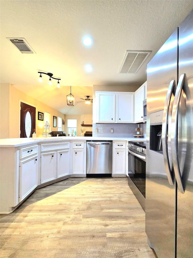 110 Red Bud St, Shepherd, TX 77371 - kitchen with stainless steel appliances, light wood finished floors, white cabinetry, a textured ceiling, and a peninsula