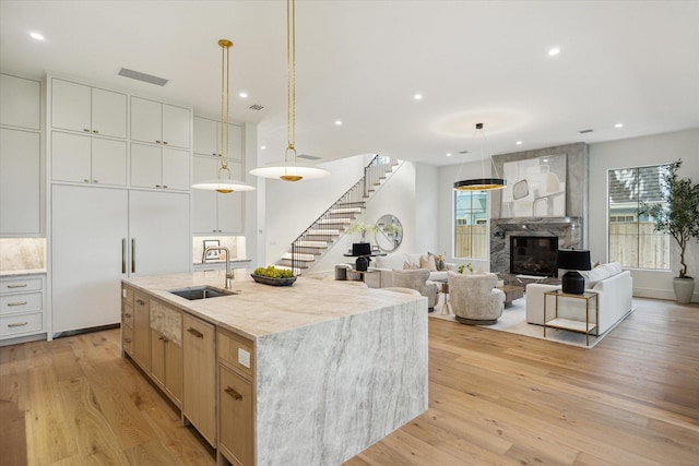 3755 Rice Blvd, Houston, TX 77005 - kitchen with light wood-type flooring, a stone fireplace, a kitchen island with sink, pendant lighting, and recessed lighting