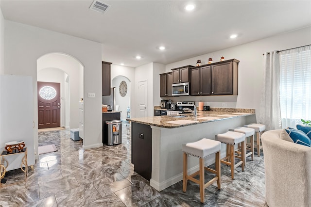 10731 Spring Brook Pass Dr, Humble, TX 77396 - kitchen featuring stainless steel appliances, arched walkways, dark brown cabinets, a kitchen breakfast bar, and recessed lighting