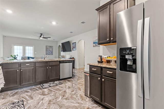 10731 Spring Brook Pass Dr, Humble, TX 77396 - kitchen with appliances with stainless steel finishes, arched walkways, a ceiling fan, dark brown cabinets, and light stone countertops