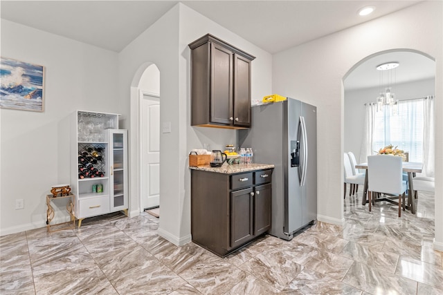 10731 Spring Brook Pass Dr, Humble, TX 77396 - kitchen featuring arched walkways, stainless steel fridge, light marble finish flooring, dark brown cabinets, and light stone countertops