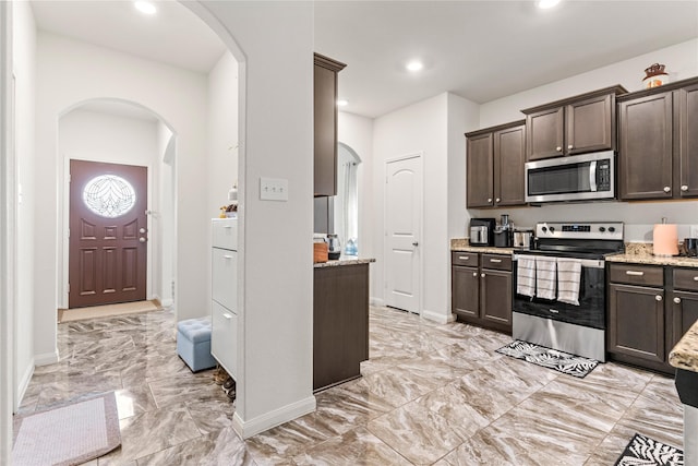 10731 Spring Brook Pass Dr, Humble, TX 77396 - kitchen with appliances with stainless steel finishes, light marble finish floors, dark brown cabinets, arched walkways, and recessed lighting