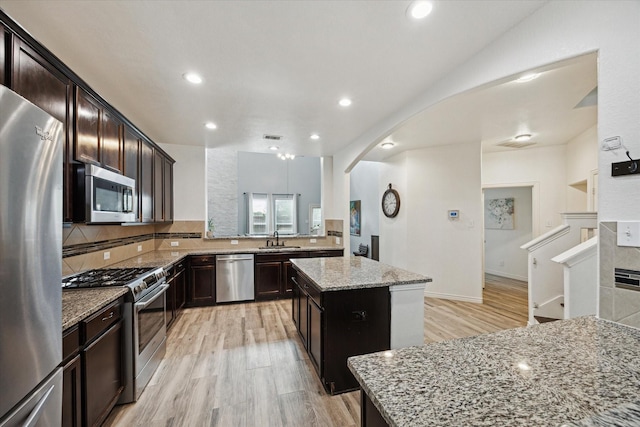 20838 Morgan Knoll Ln, Katy, TX 77449 - kitchen with stainless steel appliances, light stone counters, light wood-style flooring, a kitchen island, and arched walkways