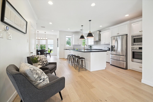 1101 Tabor St, Houston, TX 77009 - kitchen featuring appliances with stainless steel finishes, wall chimney exhaust hood, light wood-style floors, a kitchen breakfast bar, and white cabinets