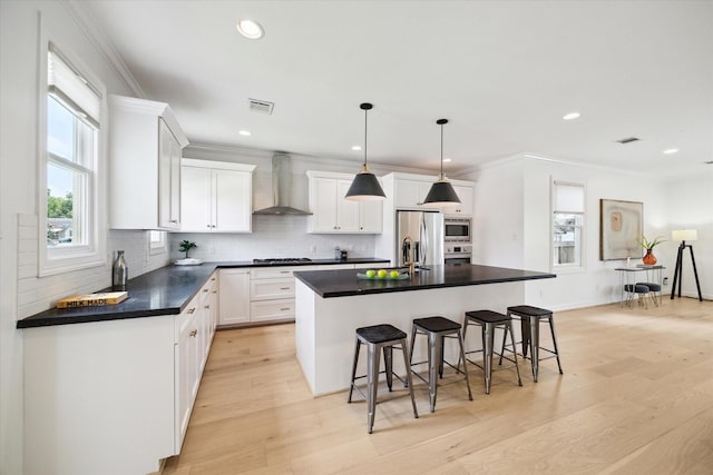 1101 Tabor St, Houston, TX 77009 - kitchen with wall chimney range hood, appliances with stainless steel finishes, light wood-type flooring, a breakfast bar, and ornamental molding
