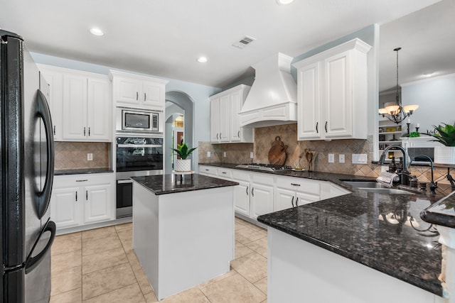 32210 Mink Creek Ct, Magnolia, TX 77355 - kitchen with appliances with stainless steel finishes, custom range hood, tasteful backsplash, a chandelier, and arched walkways