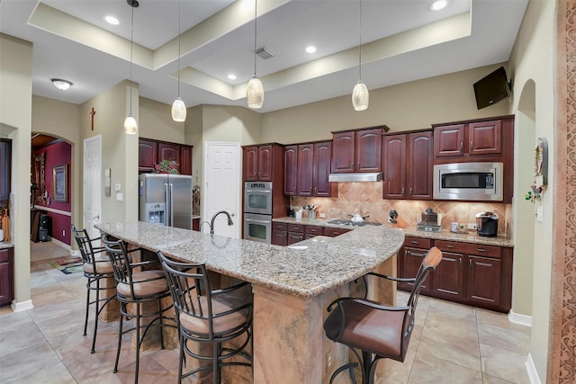 5702 Silverthorn Glen Dr, Spring, TX 77379 - kitchen with appliances with stainless steel finishes, a tray ceiling, under cabinet range hood, backsplash, and a breakfast bar area