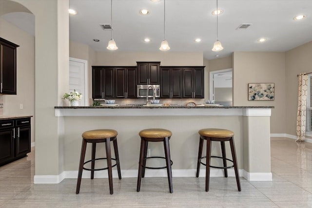 18135 Berry Garden Ln, Spring, TX 77379 - kitchen with stainless steel microwave, a kitchen bar, recessed lighting, decorative light fixtures, and dark stone counters