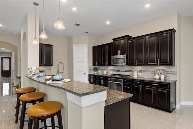 18135 Berry Garden Ln, Spring, TX 77379 - kitchen featuring stainless steel appliances, arched walkways, tasteful backsplash, a kitchen bar, and recessed lighting