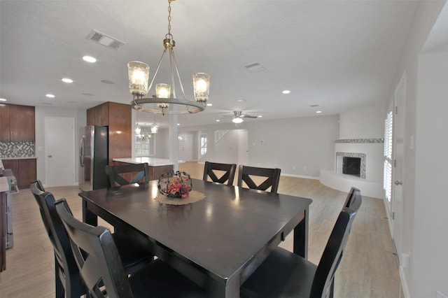 15815 Baytree Dr, Houston, TX 77070 - dining room featuring a chandelier, recessed lighting, a fireplace with raised hearth, a ceiling fan, and light wood-type flooring