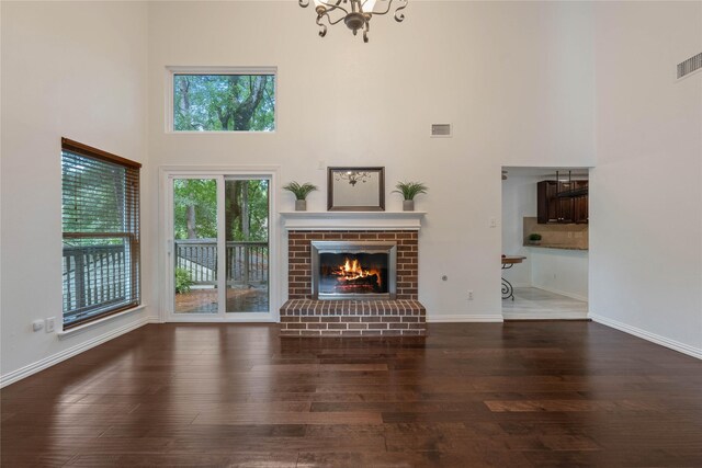 6 Sylvan Forest Dr, The Woodlands, TX 77381 - unfurnished living room with a towering ceiling, wood finished floors, a brick fireplace, and a chandelier