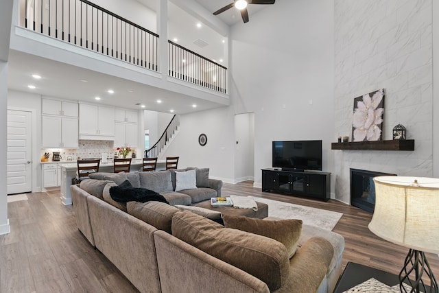 9726 Dani Lake Dr, Tomball, TX 77375 - living room featuring ceiling fan, stairway, a towering ceiling, wood finished floors, and a tiled fireplace