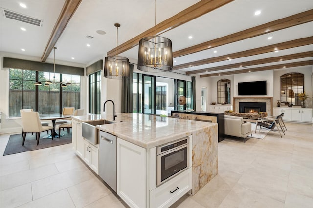 4618 Devon St, Houston, TX 77027 - kitchen with an island with sink, dishwasher, beam ceiling, a warm lit fireplace, and light stone countertops