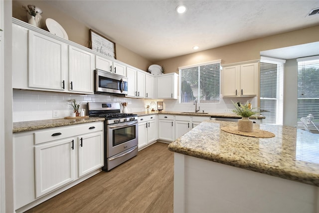 18219 Water Mill Dr, Cypress, TX 77429 - kitchen featuring appliances with stainless steel finishes, white cabinets, light wood finished floors, tasteful backsplash, and light stone countertops
