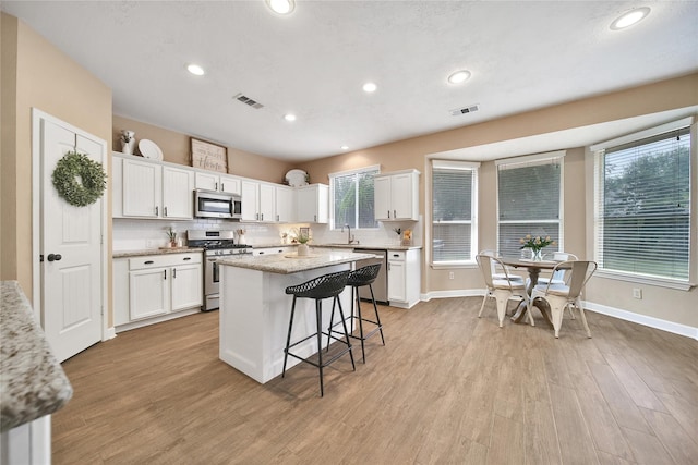 18219 Water Mill Dr, Cypress, TX 77429 - kitchen with appliances with stainless steel finishes, white cabinetry, a breakfast bar, a kitchen island, and light wood finished floors