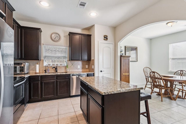 21015 Echo Manor Dr, Hockley, TX 77447 - kitchen featuring arched walkways, appliances with stainless steel finishes, backsplash, a breakfast bar area, and light stone countertops