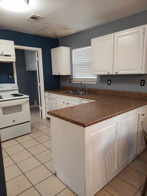 380 Rae Ann Blvd, Livingston, TX 77351 - kitchen featuring white electric range oven, dark countertops, a peninsula, white cabinets, and light tile patterned floors