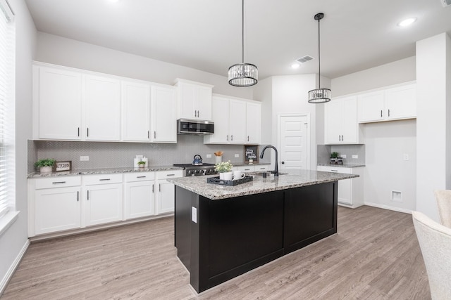 4118 Palmer Meadow Ct, Katy, TX 77494 - kitchen with stainless steel microwave, light wood-type flooring, tasteful backsplash, white cabinets, and a center island with sink