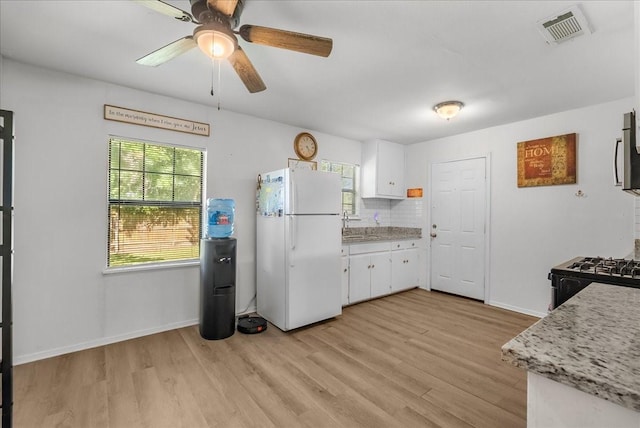 1312 22nd St N, Texas City, TX 77590 - kitchen with freestanding refrigerator, gas stove, light wood-style flooring, and white cabinets