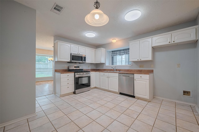 22522 Round Valley Dr, Katy, TX 77450 - kitchen with stainless steel appliances, white cabinetry, light tile patterned floors, pendant lighting, and a textured ceiling