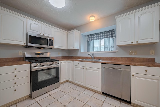 22522 Round Valley Dr, Katy, TX 77450 - kitchen featuring appliances with stainless steel finishes, white cabinetry, light tile patterned floors, a textured ceiling, and dark countertops