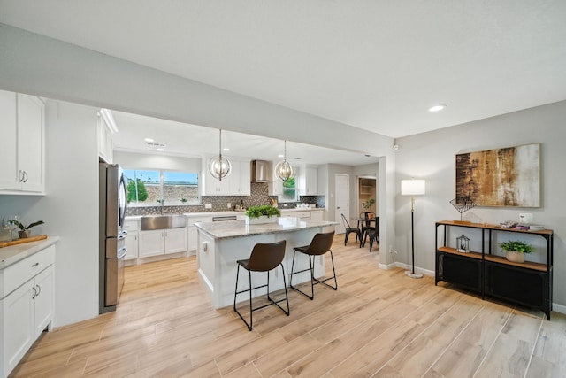 4003 Mischire Dr, Houston, TX 77025 - kitchen featuring freestanding refrigerator, wall chimney range hood, a kitchen bar, a kitchen island, and light wood finished floors