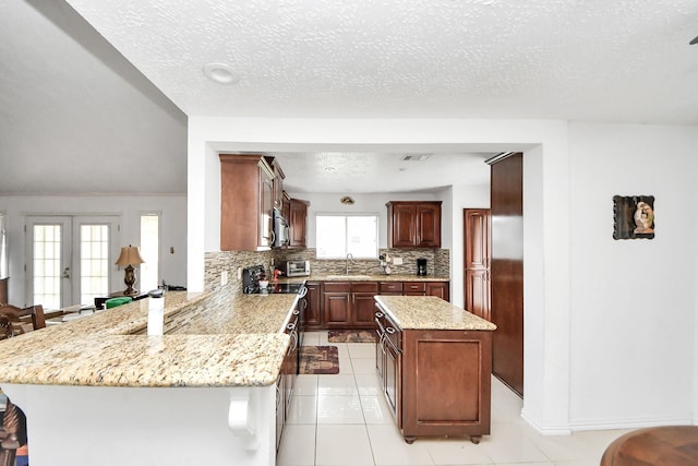 13411 Natasha Ln, Houston, TX 77015 - kitchen featuring stainless steel microwave, decorative backsplash, a peninsula, a textured ceiling, and light tile patterned floors